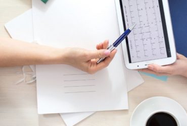 Hands exchanging a tablet with documents nearby.