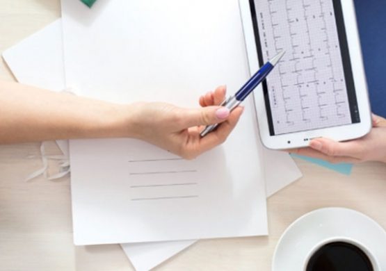 Hands exchanging a tablet with documents nearby.